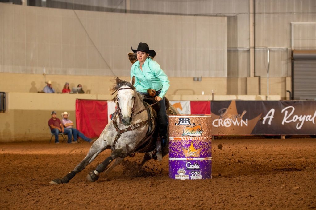 Barrel racing horse turning hard around a barrel under arena lights